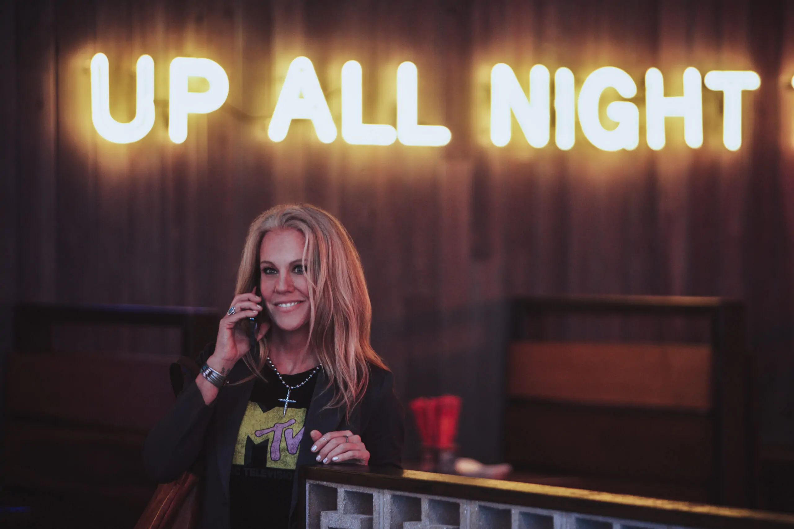 Woman talking on the phone in front of a neon 'Up All Night' sign